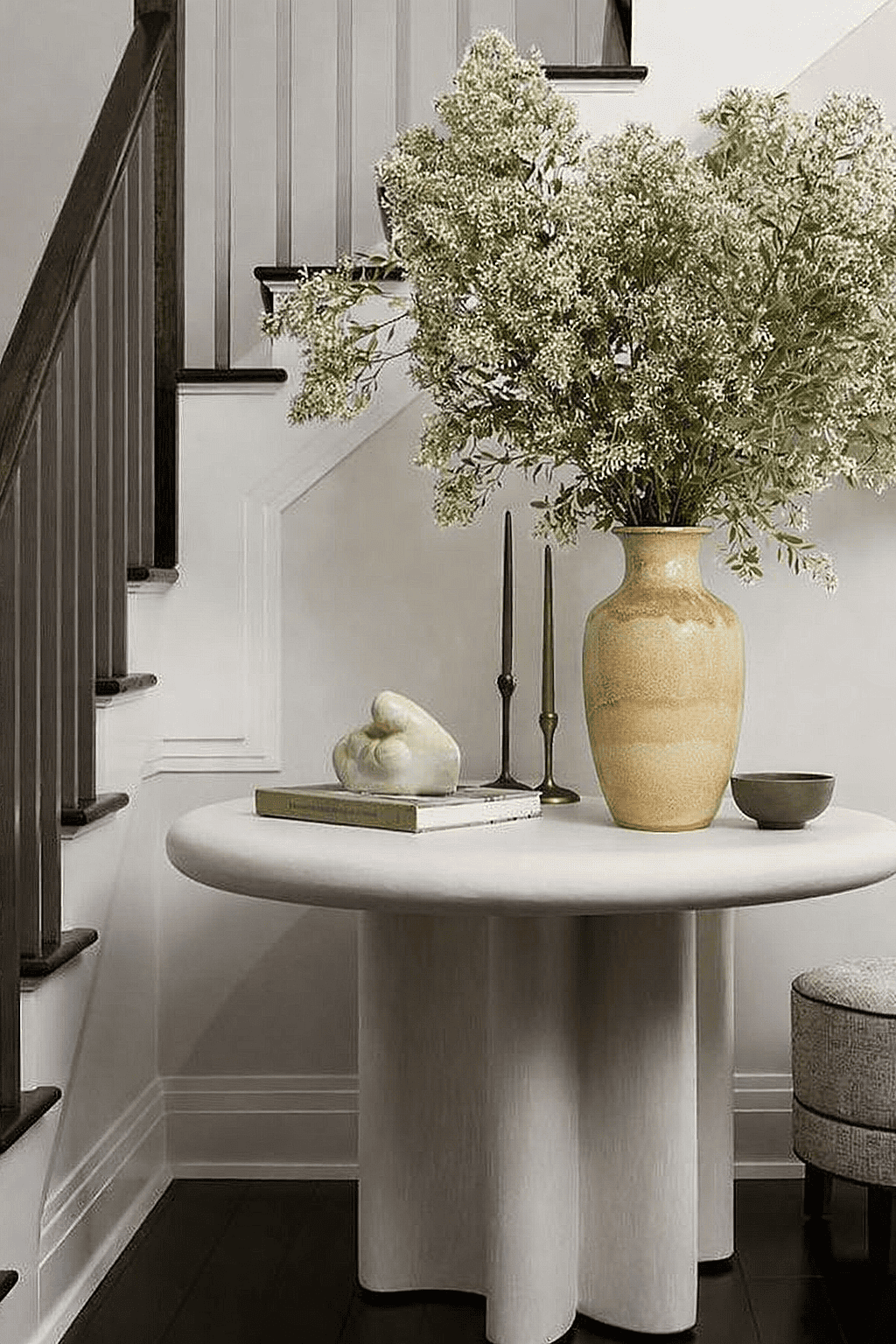 Decorative ceramic vase with floral branches styled on a round table in a house entryway near the staircase