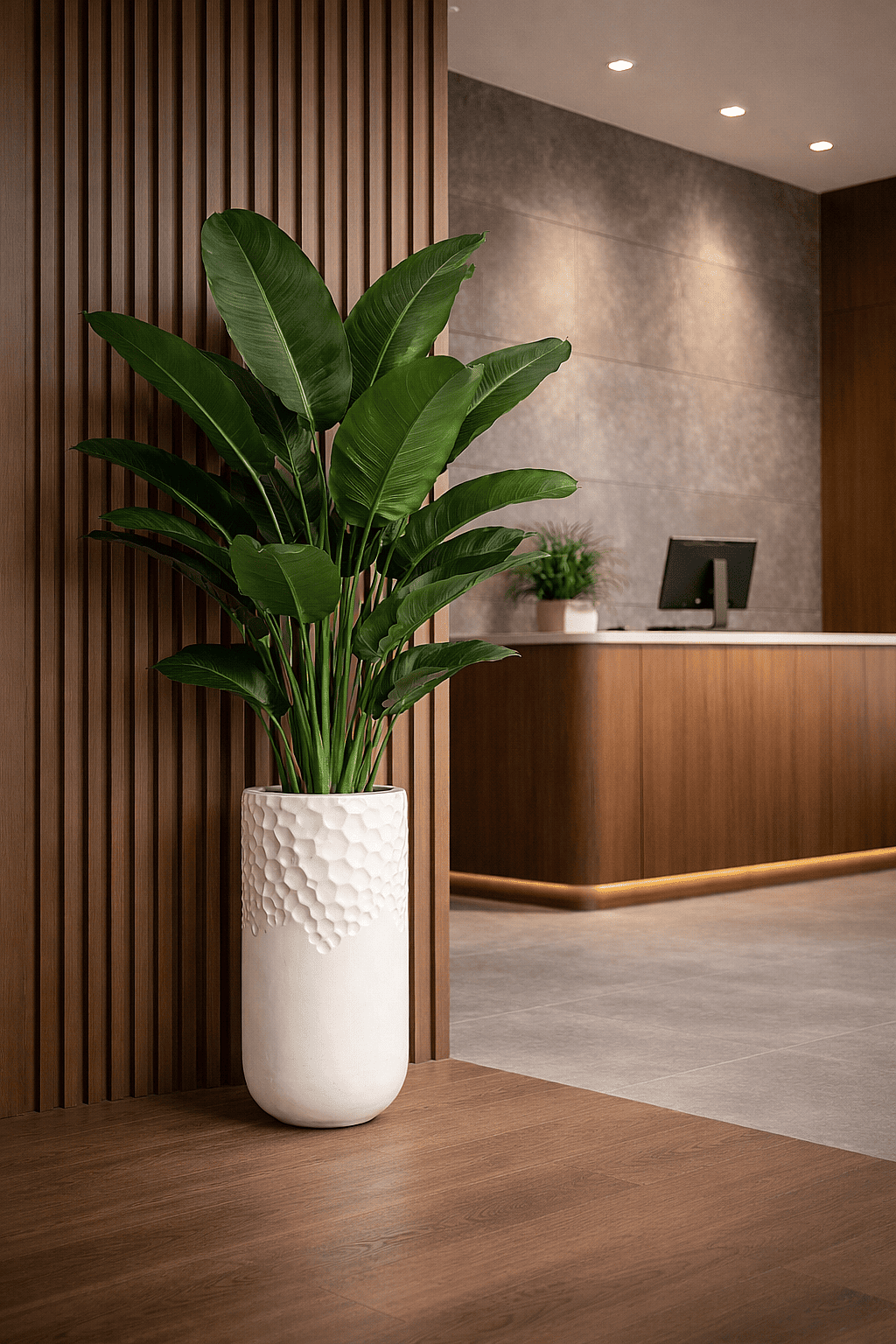Tall white textured planter with tropical plant placed beside a wooden wall in a modern hotel lobby reception area