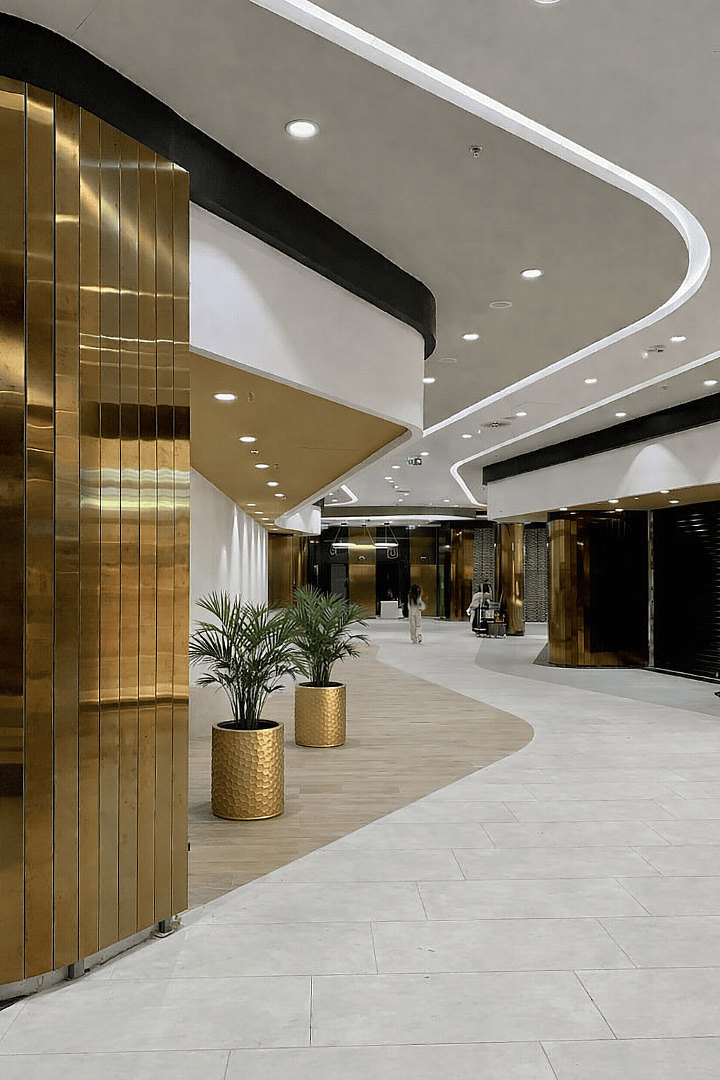 Hammered gold cylindrical planters with indoor palm plants decorating the lobby of a luxury mixed-use office and retail complex