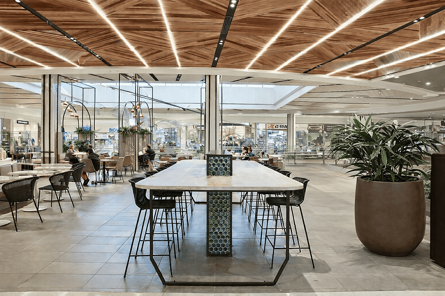 Large round planter with indoor tropical plants placed beside seating areas inside a modern mixed-use shopping mall interior