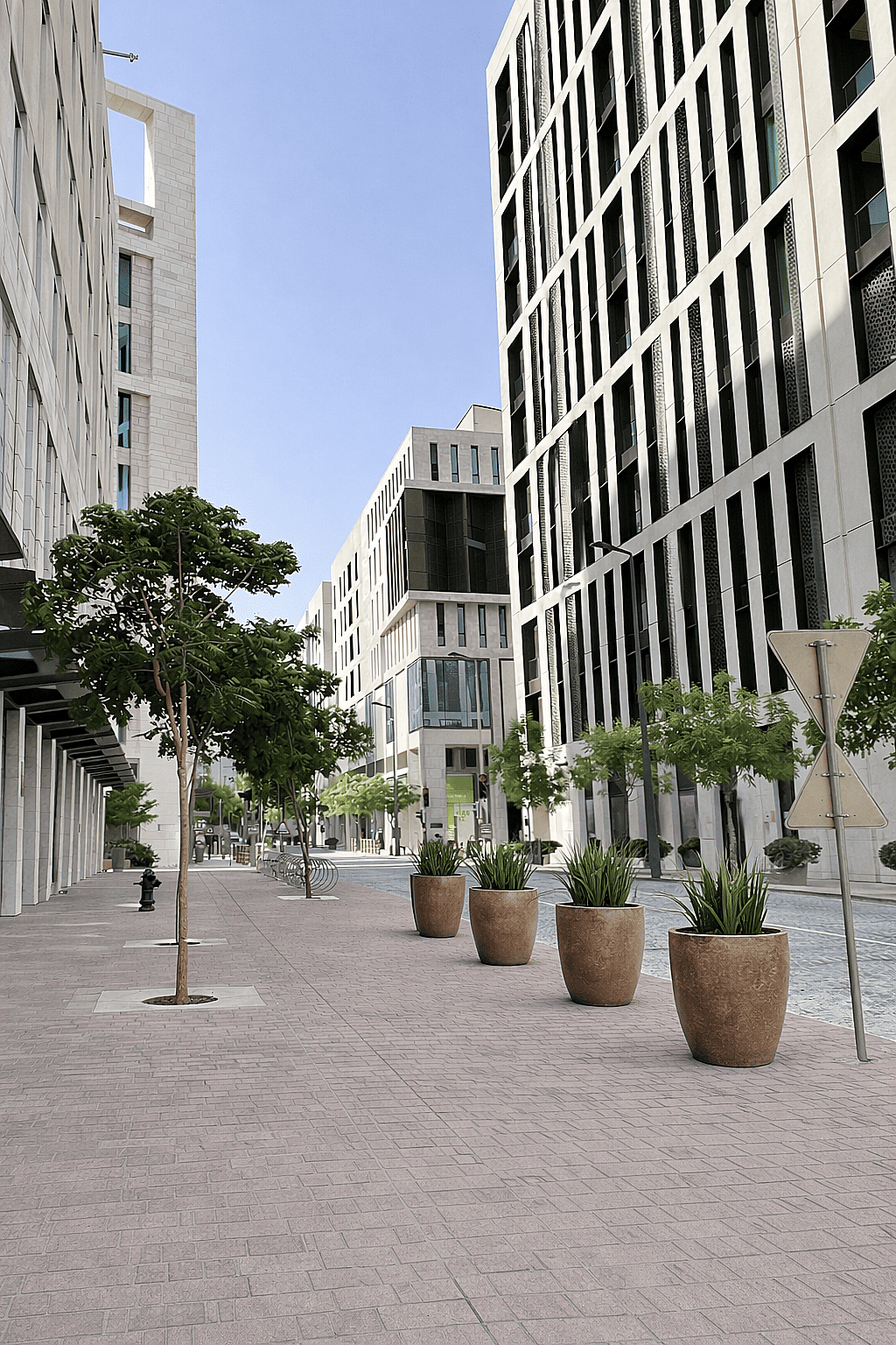 Large round outdoor planters with ornamental grasses placed along a pedestrian street in a modern mixed-use urban development surrounded by office buildings