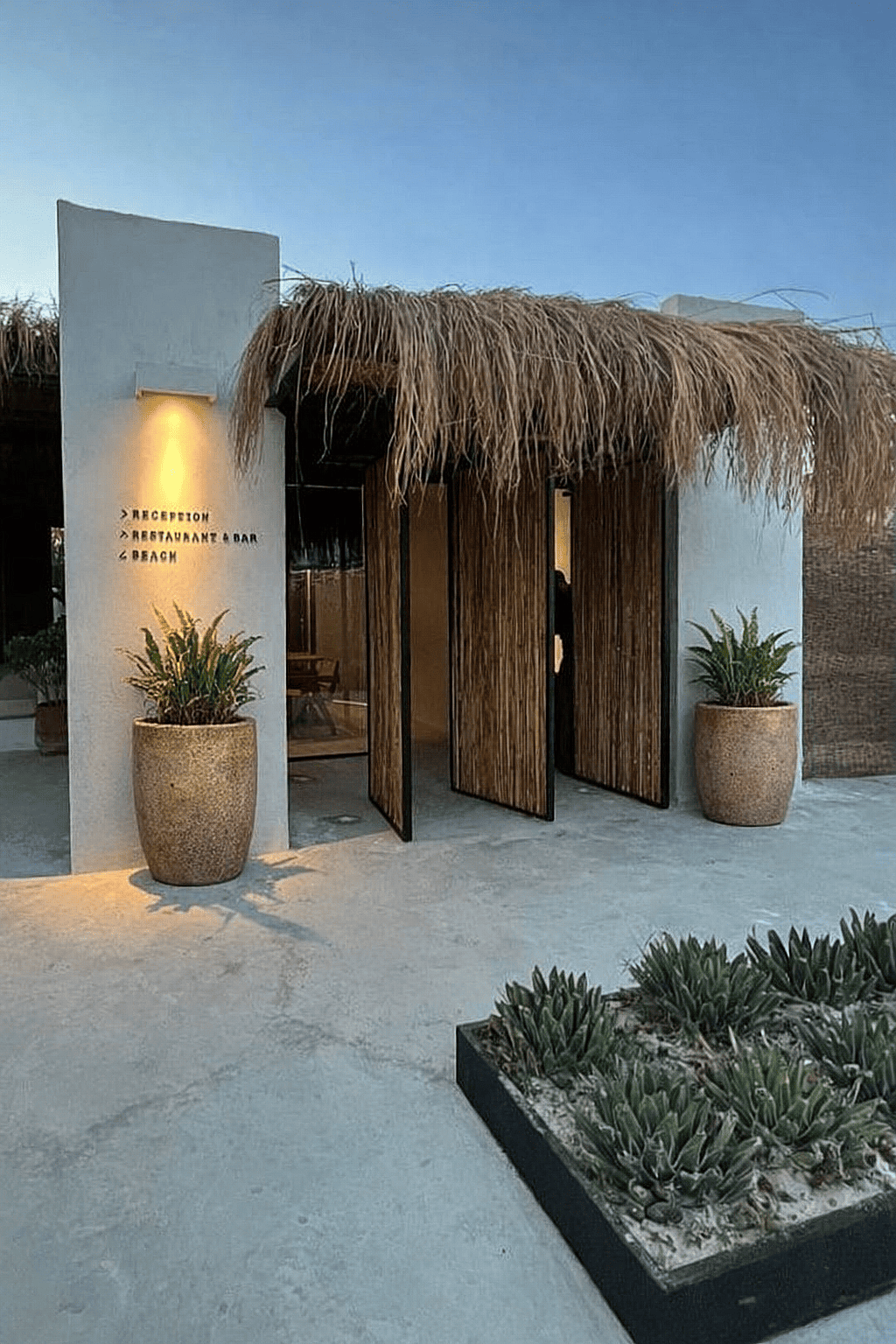 Round rustic ceramic planters with tropical plants positioned at the entrance walkway of a beach resort building