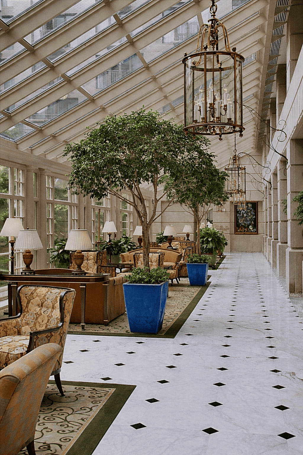 Large blue ceramic planters with indoor trees decorating a bright hotel restaurant lounge under a glass ceiling