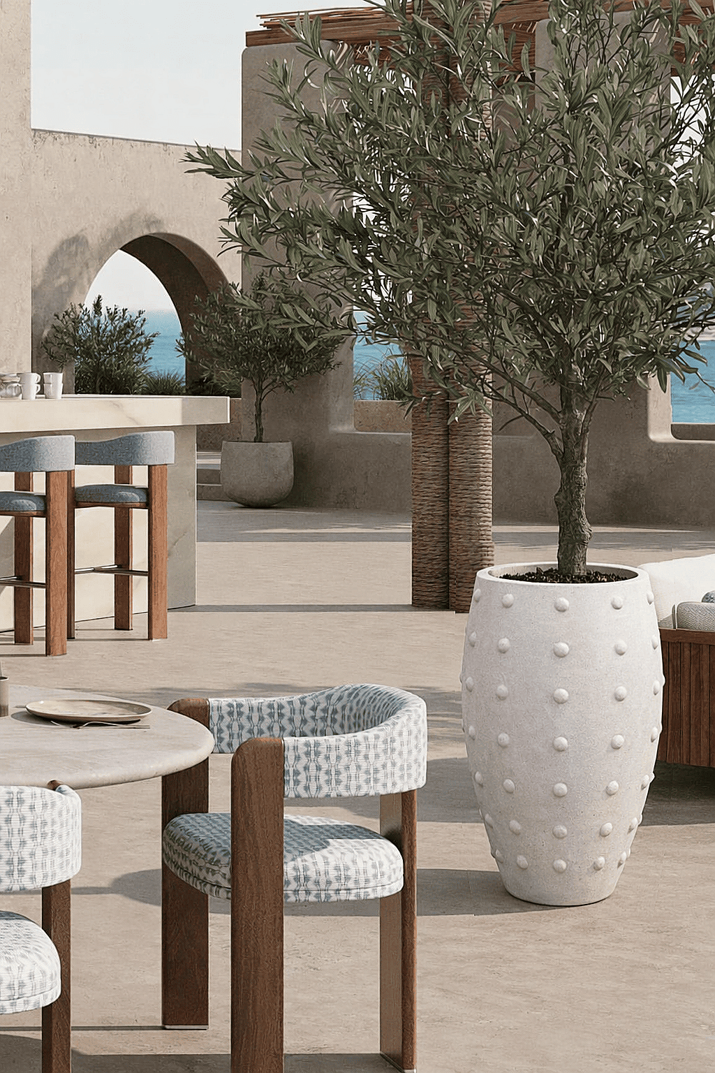 Large decorative planter with olive tree positioned on a Mediterranean style restaurant terrace overlooking the sea